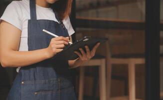 Startup successful small business owner sme beauty girl stand with tablet smartphone in coffee shop restaurant. Portrait of asian tan woman barista cafe owner. SME entrepreneur seller business concept photo