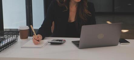 Asian Businesswoman Using laptop computer and working at office with calculator document on desk, doing planning analyzing the financial report, business plan investment, finance analysis concept. photo