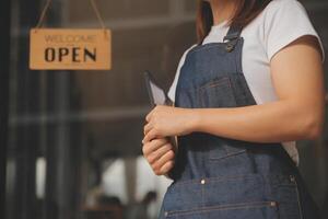 Startup successful small business owner sme beauty girl stand with tablet smartphone in coffee shop restaurant. Portrait of asian tan woman barista cafe owner. SME entrepreneur seller business concept photo