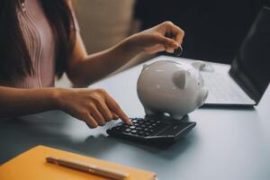 Young Asian woman saving for retirement Saving money through a piggy bank and taking notes on notebook, savings concept. photo