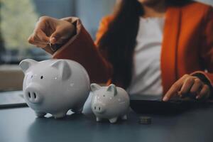 un joven niña trabajos a un computadora portátil, escribe un negocio desarrollo plan en un computadora portátil, desarrolla un estrategia y hace cálculos de ganado fondos. un mujer pone su ahorros en un cerdito banco. foto