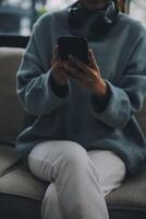 Happy pretty millennial Indian girl relaxing at home, resting in armchair, typing on smartphone, using online app, software, shopping on Internet, making video call. Mobile phone communication photo