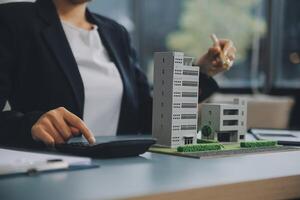 Close up realtor sit at table holds tiny house model, layout of cottage. Real estate purchase, new property, ownership, construction company make special offer to client, affordable dwelling concept photo