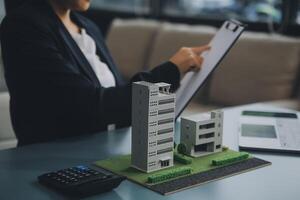 Close up realtor sit at table holds tiny house model, layout of cottage. Real estate purchase, new property, ownership, construction company make special offer to client, affordable dwelling concept photo