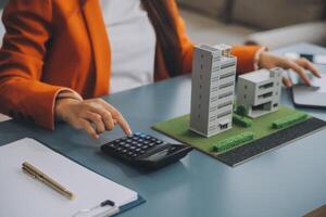 Close up realtor sit at table holds tiny house model, layout of cottage. Real estate purchase, new property, ownership, construction company make special offer to client, affordable dwelling concept photo