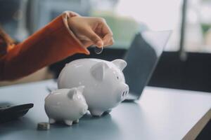 A young girl works at a laptop, writes a business development plan in a notebook, develops a strategy and makes calculations of earned funds. A woman puts her savings in a piggy bank. photo