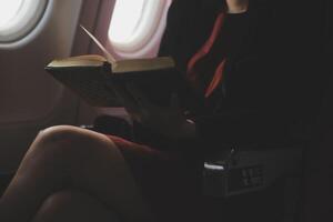 Blonde female tourist checking incoming notification on smartphone sitting on seat of airplane with netbook.Young businesswoman share media from telephone on laptop computer during plane flight photo