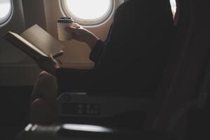 Blonde female tourist checking incoming notification on smartphone sitting on seat of airplane with netbook.Young businesswoman share media from telephone on laptop computer during plane flight photo