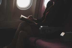 Blonde female tourist checking incoming notification on smartphone sitting on seat of airplane with netbook.Young businesswoman share media from telephone on laptop computer during plane flight photo