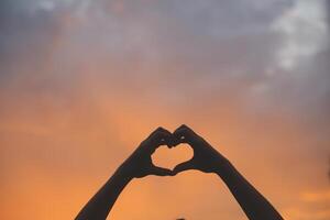 Silhouette of hands in heart symbol around the sun photo