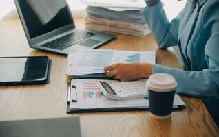 Asian Businesswoman Using laptop computer and working at office with calculator document on desk, doing planning analyzing the financial report, business plan investment, finance analysis concept. photo
