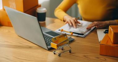 mujer joven dueña de una pequeña empresa comprando en línea en casa. tomando nota de los pedidos de los clientes con teléfonos móviles. pyme emprendedor o concepto de estilo de vida independiente. foto