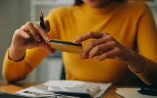 joven mujer participación un teléfono inteligente, tableta demostración pago éxito y crédito tarjeta con amarillo paquete o empaquetar caja como en línea compras concepto en oficina foto