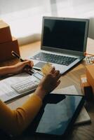 joven mujer participación un teléfono inteligente, tableta demostración pago éxito y crédito tarjeta con amarillo paquete o empaquetar caja como en línea compras concepto en oficina foto