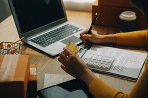 joven mujer participación un teléfono inteligente, tableta demostración pago éxito y crédito tarjeta con amarillo paquete o empaquetar caja como en línea compras concepto en oficina foto