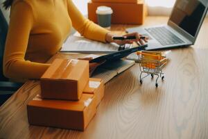 mujer joven dueña de una pequeña empresa comprando en línea en casa. tomando nota de los pedidos de los clientes con teléfonos móviles. pyme emprendedor o concepto de estilo de vida independiente. foto