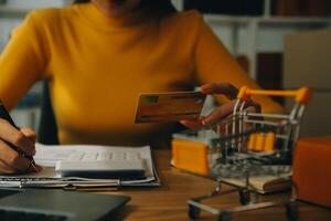 joven mujer participación un teléfono inteligente, tableta demostración pago éxito y crédito tarjeta con amarillo paquete o empaquetar caja como en línea compras concepto en oficina foto