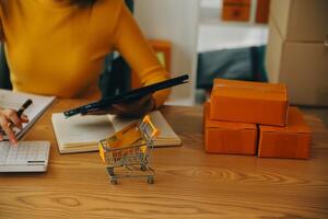 mujer joven dueña de una pequeña empresa comprando en línea en casa. tomando nota de los pedidos de los clientes con teléfonos móviles. pyme emprendedor o concepto de estilo de vida independiente. foto