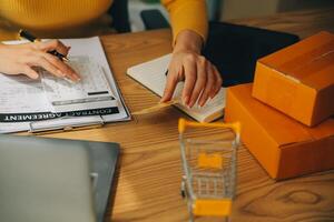 joven mujer participación un teléfono inteligente, tableta demostración pago éxito y crédito tarjeta con amarillo paquete o empaquetar caja como en línea compras concepto en oficina foto