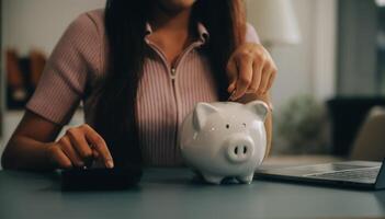 joven asiático mujer ahorro para Jubilación ahorro dinero mediante un cerdito banco y tomando notas en computadora portátil, ahorros concepto. foto