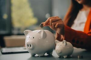 A young girl works at a laptop, writes a business development plan in a notebook, develops a strategy and makes calculations of earned funds. A woman puts her savings in a piggy bank. photo