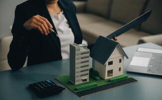 Close up realtor sit at table holds tiny house model, layout of cottage. Real estate purchase, new property, ownership, construction company make special offer to client, affordable dwelling concept photo