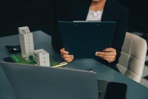 Close up realtor sit at table holds tiny house model, layout of cottage. Real estate purchase, new property, ownership, construction company make special offer to client, affordable dwelling concept photo