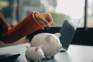 A young girl works at a laptop, writes a business development plan in a notebook, develops a strategy and makes calculations of earned funds. A woman puts her savings in a piggy bank. photo