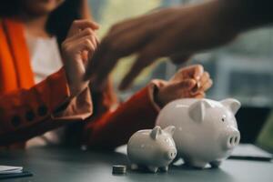 A young girl works at a laptop, writes a business development plan in a notebook, develops a strategy and makes calculations of earned funds. A woman puts her savings in a piggy bank. photo