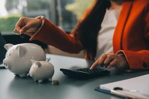 A young girl works at a laptop, writes a business development plan in a notebook, develops a strategy and makes calculations of earned funds. A woman puts her savings in a piggy bank. photo