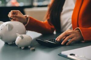 A young girl works at a laptop, writes a business development plan in a notebook, develops a strategy and makes calculations of earned funds. A woman puts her savings in a piggy bank. photo