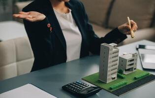 Close up realtor sit at table holds tiny house model, layout of cottage. Real estate purchase, new property, ownership, construction company make special offer to client, affordable dwelling concept photo