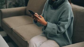 Happy pretty millennial Indian girl relaxing at home, resting in armchair, typing on smartphone, using online app, software, shopping on Internet, making video call. Mobile phone communication photo