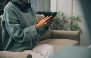 Happy pretty millennial Indian girl relaxing at home, resting in armchair, typing on smartphone, using online app, software, shopping on Internet, making video call. Mobile phone communication photo