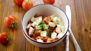 Salat von frisch reif Tomaten mit Mozzarella und Gewürze im ein Schüssel auf ein hölzern Tabelle video