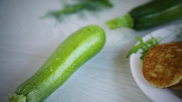 fried vegetable pancakes from squash and zucchini with herbs, on a light wooden table. video