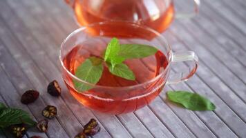 elaborada rosa mosqueta té en un vaso tetera con rosa mosqueta flores y menta, en un de madera mesa. video