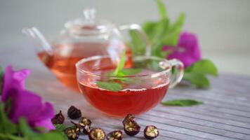 brewed rosehip tea in a glass teapot with rosehip flowers and mint, on a wooden table. video