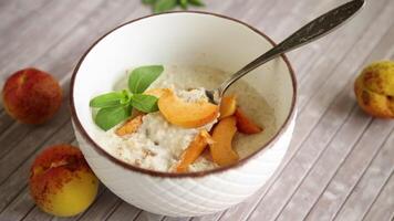 Healthy breakfast of boiled oatmeal with fresh apricots in a bowl on the table. video