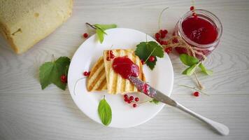 fried bread croutons for breakfast with redcurrant jam in a plate with berries on a wooden table. video