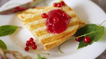 fried bread croutons for breakfast with redcurrant jam in a plate with berries on a wooden table. video