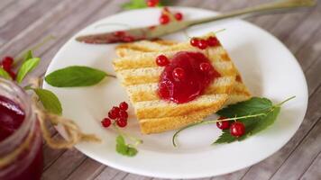 fried bread croutons for breakfast with redcurrant jam in a plate with berries on a wooden table. video