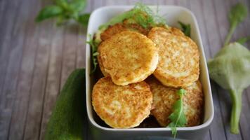 fried vegetable pancakes from squash and zucchini with herbs, on a light wooden table. video