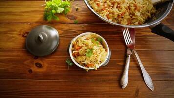 Braised cabbage with carrots, onions and herbs in a ceramic bowl on a wooden table. video