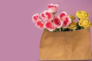 Bouquet of pink and yellow tulips in a paper bag on a purple background with copy space for your text photo