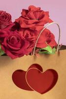 Red roses inside the brown paper shopping bag with two red hearts printed on the gift bag on a pink background photo