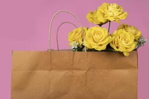 Bouquet of yellow roses in a paper bag on a pink background, valentine's day background photo