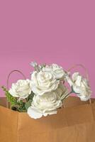 Bouquet of white roses in a paper bag on a pink background, valentine's day background photo