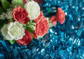 Close up of artificial red and white rose flowers on blue tinsel background. Selective focus. photo