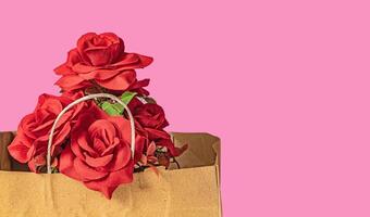 Bouquet of red roses in a brown paper bag on a pink background for Valentine's Day with copy space for your text. photo